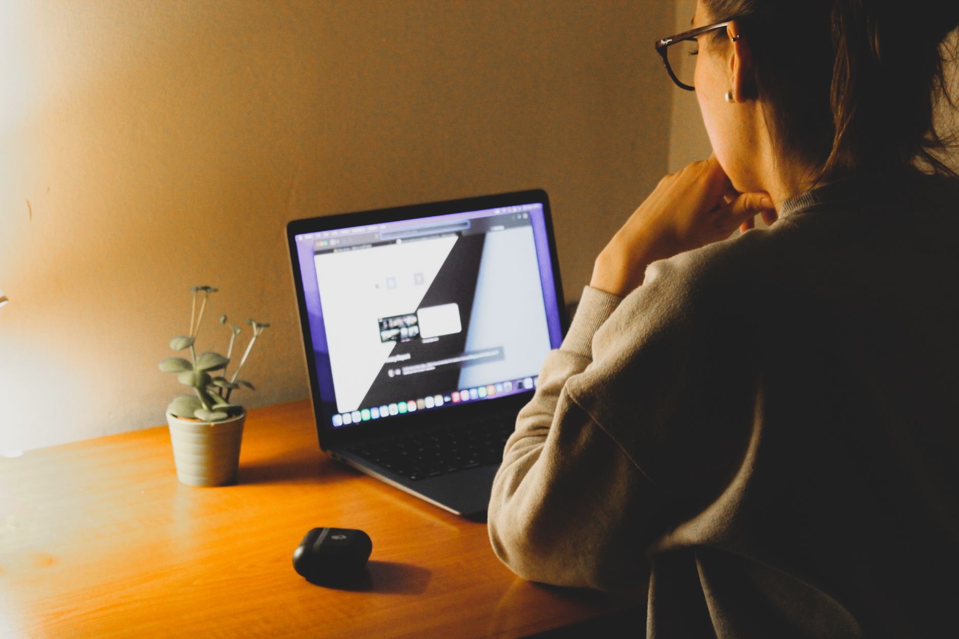 A woman working on a laptop at a wooden desk with warm lighting